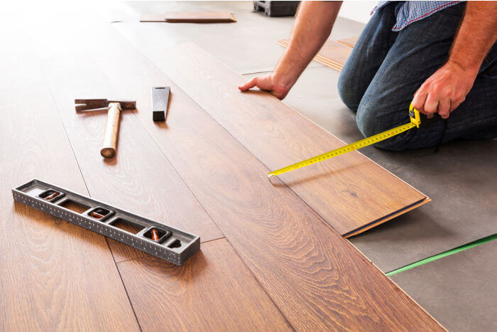 Worker measuring and installing wooden laminate flooring with tools